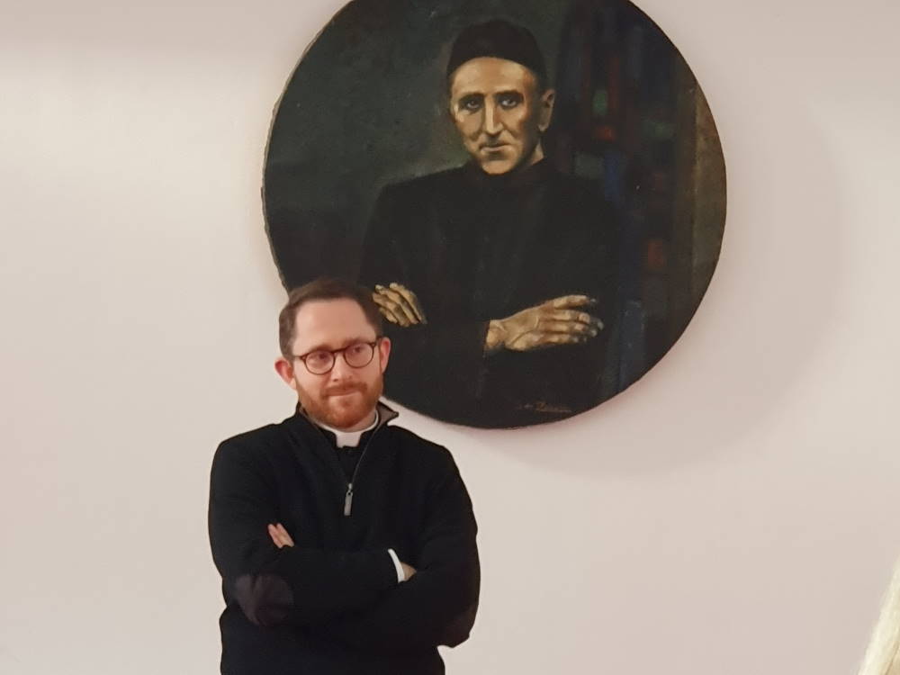un prêtre devant un portrait d'un autre prêtre